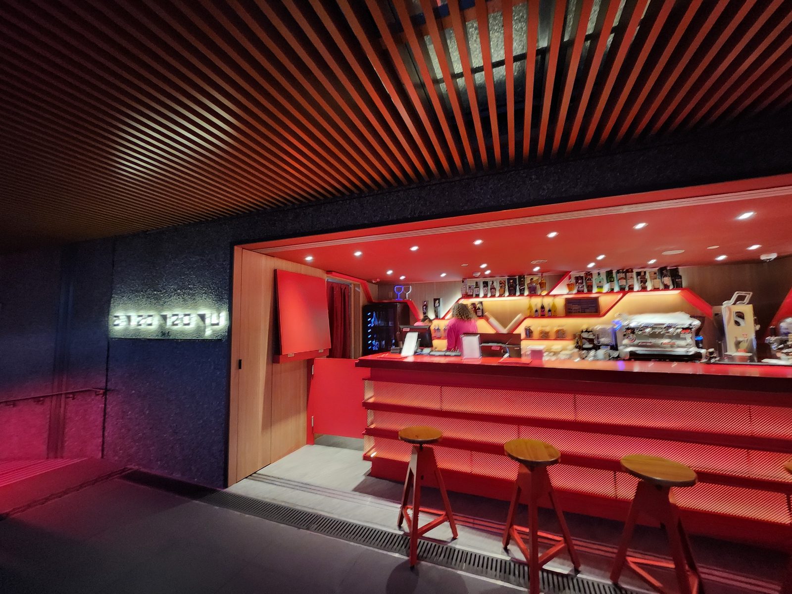 夜間酒吧正面,發光店名招牌與紅光吧檯、一整排高腳凳
